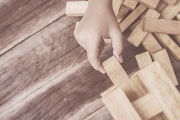 Hand holding blocks wood game (jenga) on wooden plank background