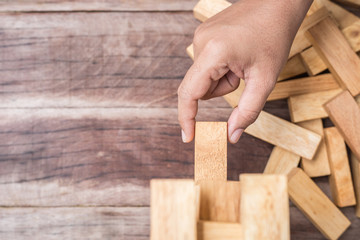 Hand holding blocks wood game (jenga) on wooden plank background