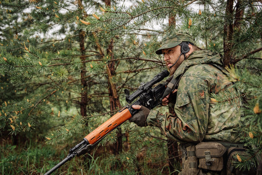 army soldier holding sniper rifle with scope and aiming in forest. war, army, technology and people concept


