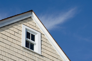 House peak with tan wooden siding and a white wood frame window against a beautiful blue sky.