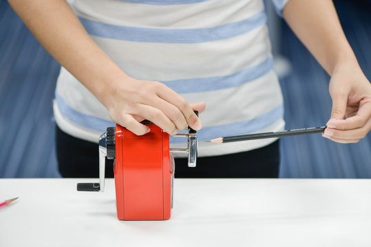 Woman is sharpening the pencil with red sharpener