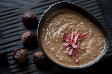 Ceramic bowl with chestnut cream-soup topped with smoked meat
