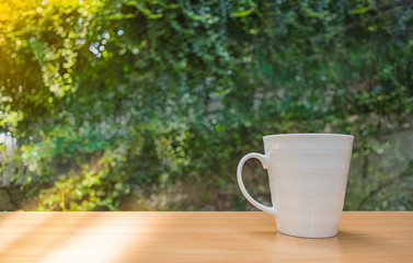 a selective focus picture of a cup of coffee on wooden table in green garden