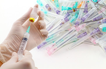 Hands of the doctor filling a vaccine syringe and many used syringes and needle on white background.