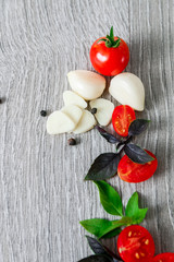 Cherry tomatoes, garlic and fresh basil on grey wooden  background. Frame. Copy space.