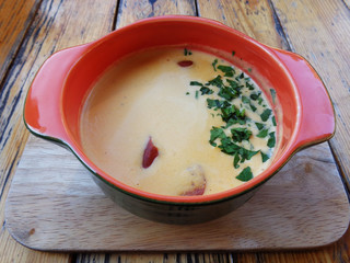 Delicious French cheese soup with smoked sausage in ceramic orange bowl,which stands on a wooden board