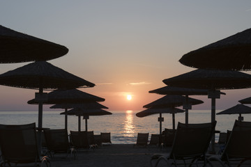 Romantic sunset on the evening beach in Greece, Chalkidiki, parasols and camp beds arround