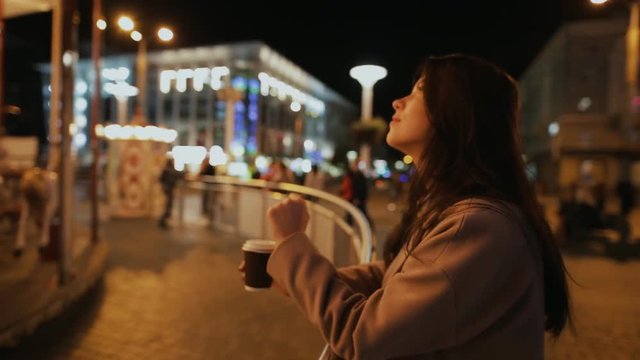 Woman walking in night city and contemplate illuminated carousel