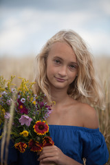 The girl in the blue dress in a field with  bouquet of flowers