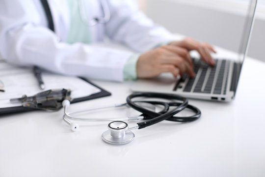 Close-up of stethoscope is lying on the table near female doctor typing on laptop computer