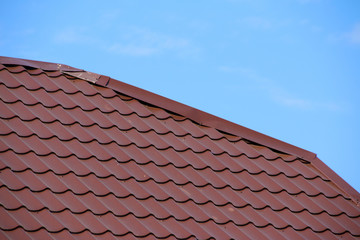 Modern roof covered with tile effect PVC coated brown metal roof sheets against a blue sky
