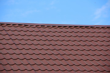 Modern roof covered with tile effect PVC coated brown metal roof sheets against a blue sky