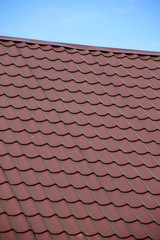 Modern roof covered with tile effect PVC coated brown metal roof sheets against a blue sky