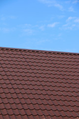 Modern roof covered with tile effect PVC coated brown metal roof sheets against a blue sky