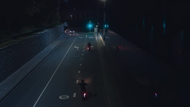 MED OVERHEAD shot of a group of bikers ride vintage cafe racer motorcycles in the streets at night. 60 FPS