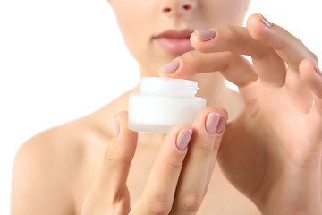 Beautiful young woman holding facial cream on white background