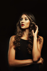 Fototapeta premium Beautiful young woman with make up and long wavy hair on black background