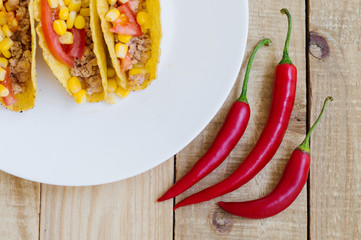 Three spicy chili peppers and mexican tacos on wooden background