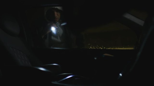 Abstract angle of thief looking into a locked car for valuables at night