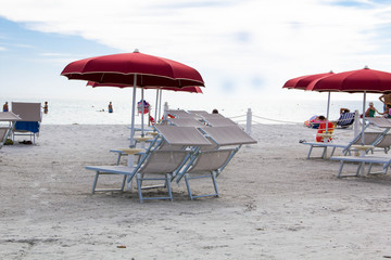 Sunbeds with umbrellas on beautiful beach of Porto Giunco and unidentified man bathing in sea, Sardinia island, Italy