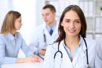 Young beautiful female doctor smiling  on the background with patient  in hospital. High level and quality medical service concept.