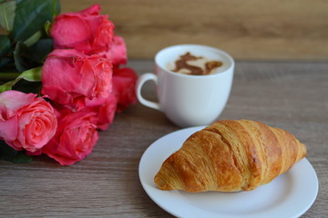 cup of cappuccino and yummy croissant with roses on the table
