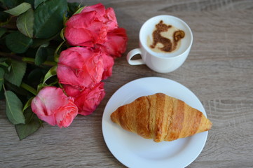 cup of cappuccino and yummy croissant with roses on the table