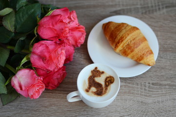cup of cappuccino and yummy croissant with roses on the table