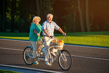 Senior couple riding tandem bike. People ride on the road. Spin the pedals faster. Race with the time.