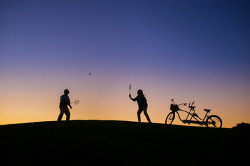Fototapeta na wymiar Couple is playing badminton. People on evening sky background. Play until you win. Test of endurance.