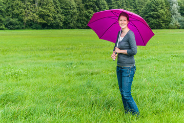Woman with pink umbrella standing on a green meadow, looking at camera