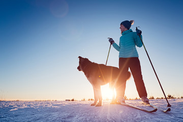 Woman skiing in a winter field with the dog