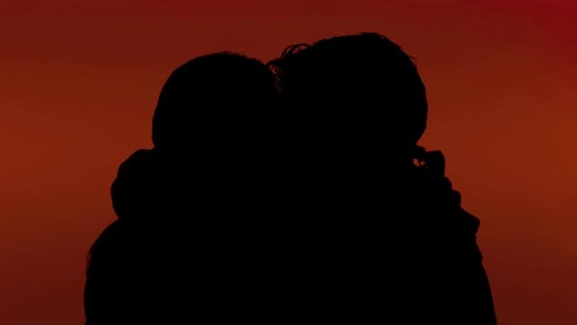 A man and a woman intensely kissing, touching each other with passion (foreplay). Silhouette shot, red background. Love, lovers, Valentine.

