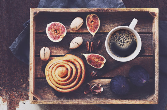 Breakfast tray with black coffee, cinnamon roll, fresh figs and pecan nuts