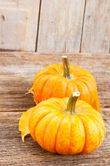 two orange pumpkins with fall leaves on wooden textured table
