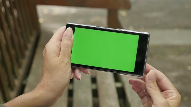 Female on the bench holding chroma key green screen phone 4K 2160p 30fps UHD footage - Caucasian woman in the park with greenscreen display tablet 3840X2160 UltraHD video 