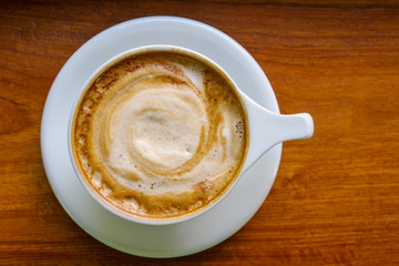 Top view of cappuccino coffee cup with milk foam on wood table background.