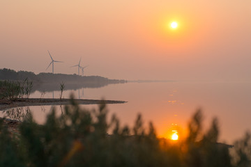 Fototapeta na wymiar Sunrise over the sea bay. Wind power station on the background