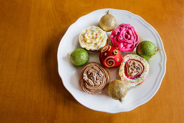 Christmas baubles with homemade cup cakes on wooden background
