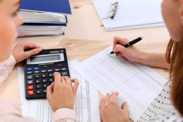 Two female accountants counting on calculator income for tax form completion hands closeup. Internal Revenue Service inspector checking financial document. Planning budget, audit  concept