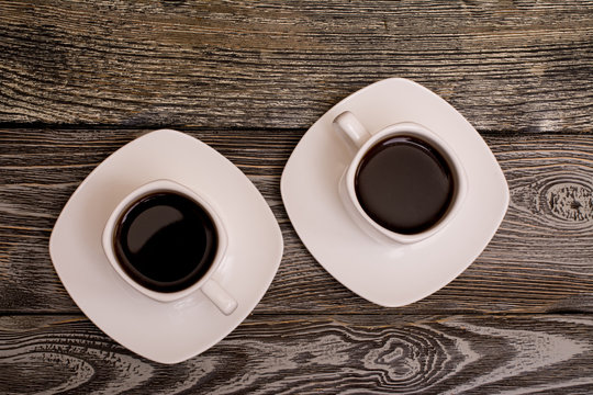 two small white cups of coffee on wooden background