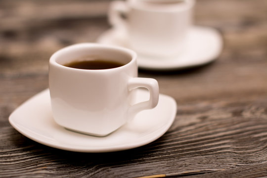 two small white cups of coffee on wooden background