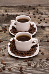two small white cups of coffee with cocoa beans on wooden background