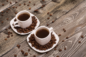 two small white cups of coffee with cocoa beans on wooden background