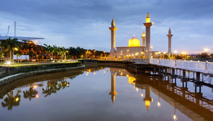 View of Bukit Jelutong Mosque with reflections of the mosque and bridge crossing over the pond during sunrise.
