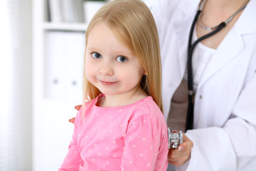 Pediatrician is taking care of baby in hospital. Little girl is being examine by doctor by stethoscope. Health care, insurance and help concept.