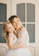 Mother and daughter like brides in white dress huging.