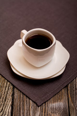 small white cup of coffee on grey fabric on wooden background