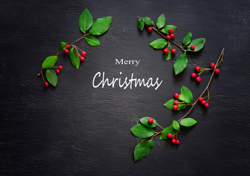 Christmas greeting card, green branches with red  berries set in a frame around greeting text on dark background