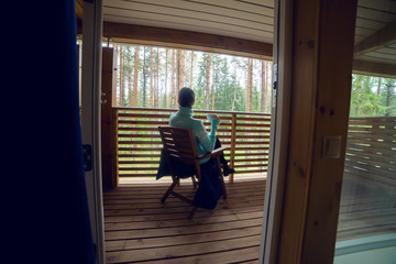 girl in a blue sweater sitting on  wooden chair and drinking tea